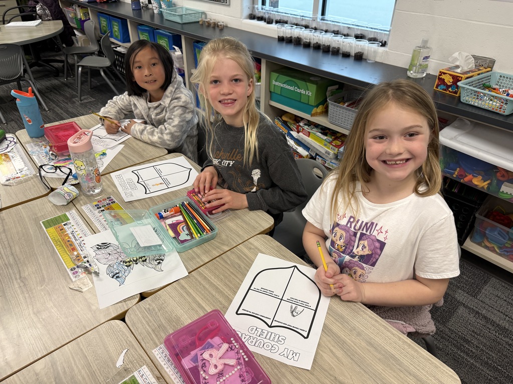 Three girls sit at desks working on their Courage Shield.