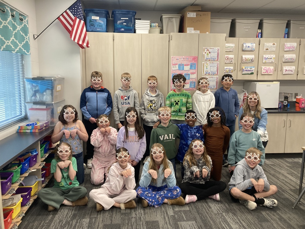 Three rows of fourth graders have on white bunny ear glasses and are smiling for a picture.