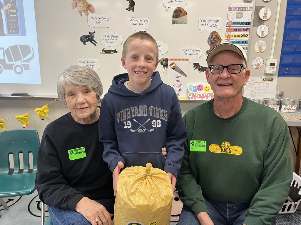 An older man and woman, both wearing "Gretna Visitor" badges, pose with a young boy holding a large yellow bag of popcorn.