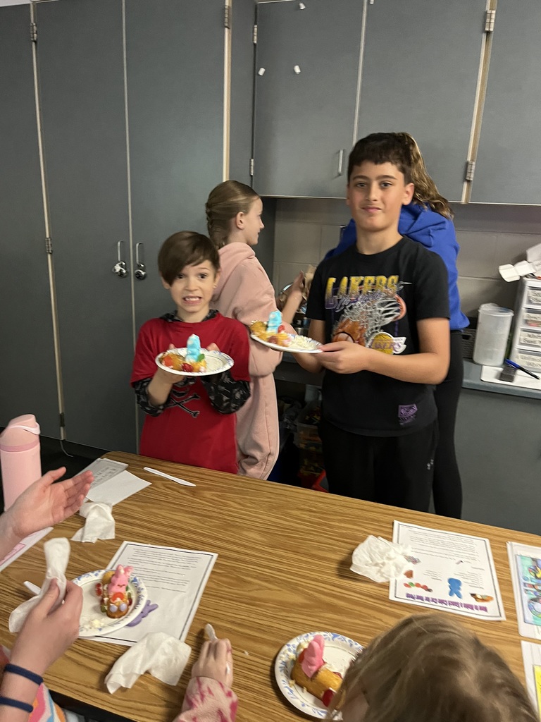 Two boys stand in a classroom holding paper plates with snack cake cars featuring blue Peeps.