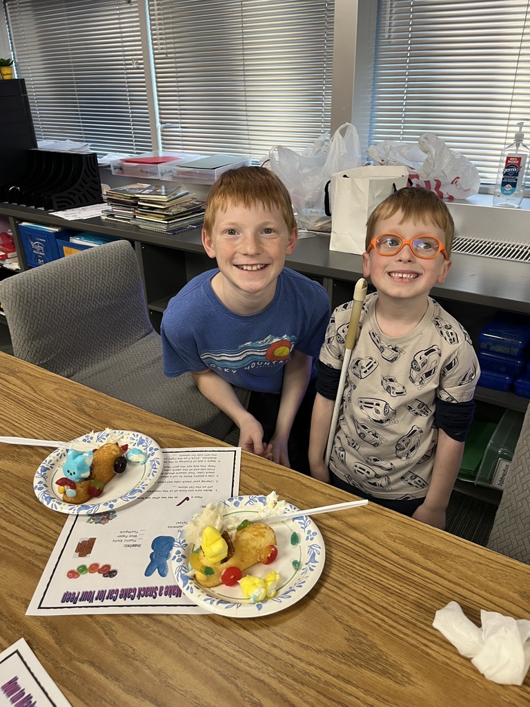 Two boys smile at a desk featuring two snack cake cars and a "How to Make a Snack Cake Car" worksheet.