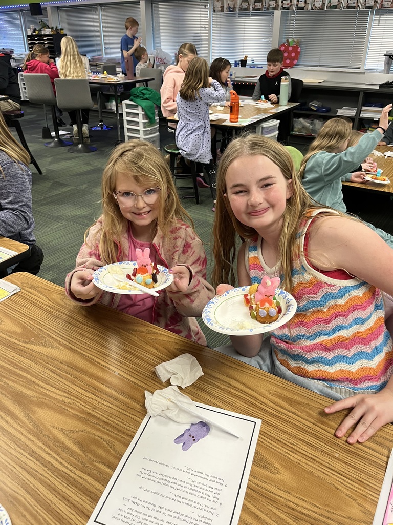 Two girls sit at a long table holding their Peep-topped snack cake creations; a set of instructions lies on the table.