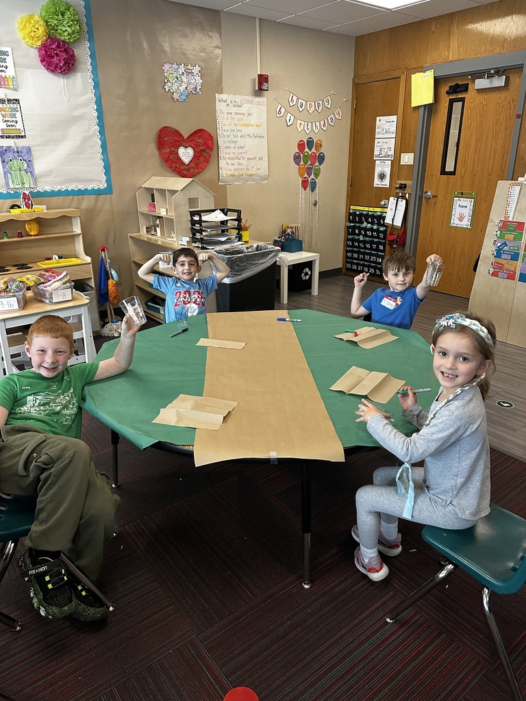 Four children pose at their craft table, smiling and showing off their decorated plastic cups.