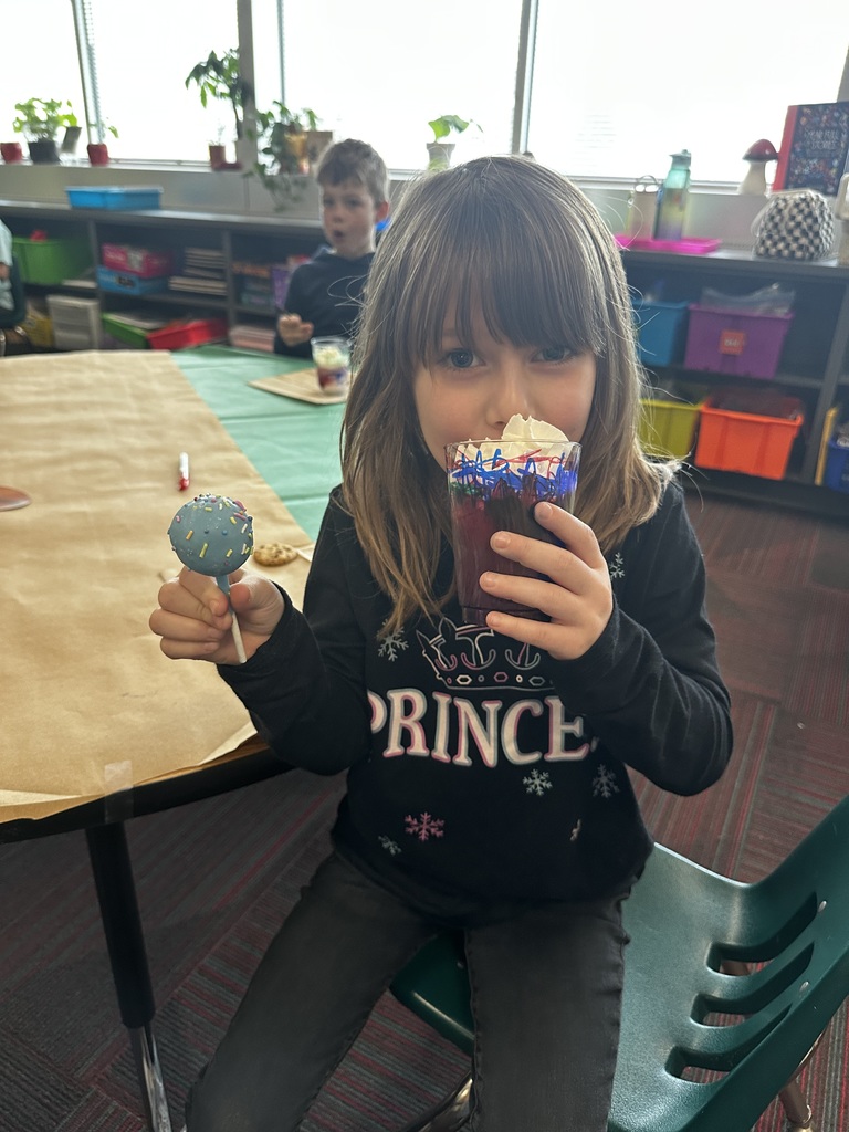 A girl in a "Princess" shirt holds up a blue cake pop and a decorated cup topped with whipped cream.