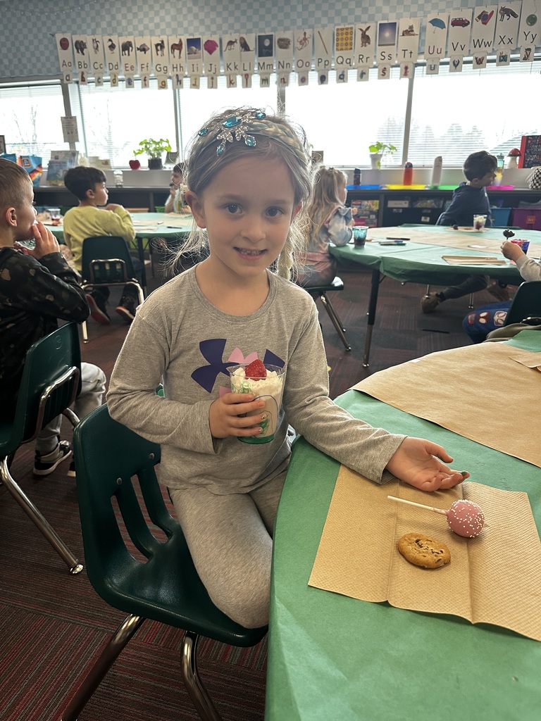 A girl wearing a blue snowflake headband holds her decorated cup treat at a classroom table.