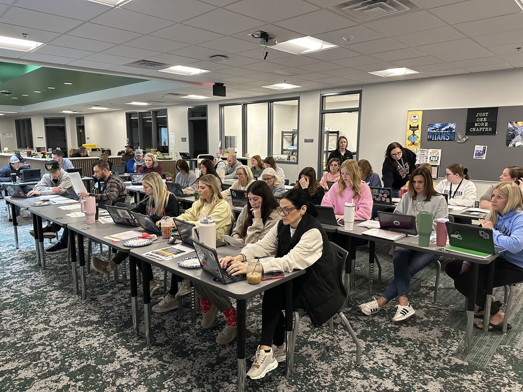 A group of teachers sit at desks working on their laptops. 