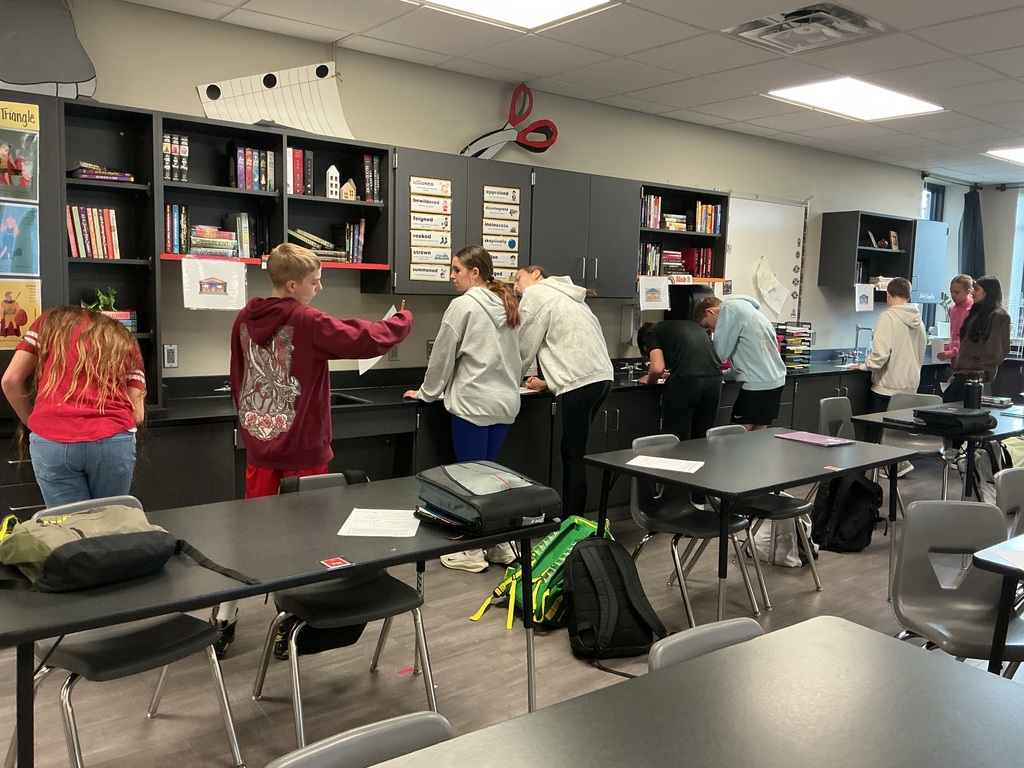 Photo of students moving around the classroom identify which Greek gods go with which cabin photos hanging on the walls.