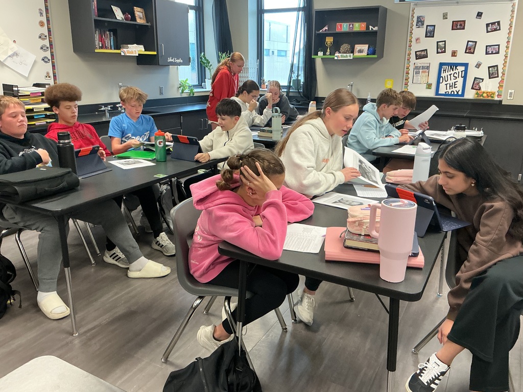 Photo of many students in a classroom collaborating in small groups do complete a sorting activity.