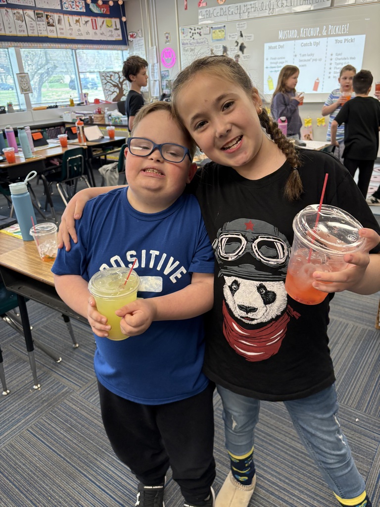 A boy in a blue "Positive" shirt and a girl in a black panda t-shirt posing with their arms around each other, each holding a colorful iced drink.