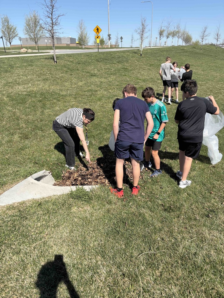 Photo of Mrs. Jones and her students picking up trash. Mrs. Jones is pointing something out to the students.