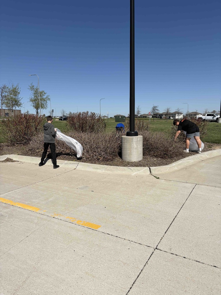 Photo of two students holding trash bags and picking up trash in the landscaping.