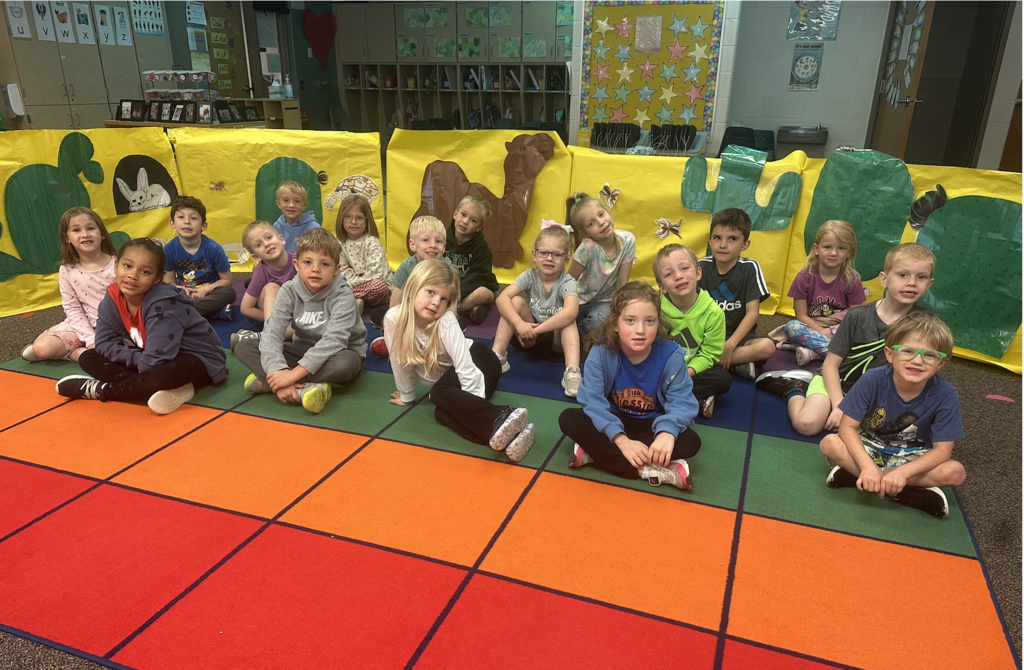 Students are sitting on a rug in front of a desert themed habitat rotation.