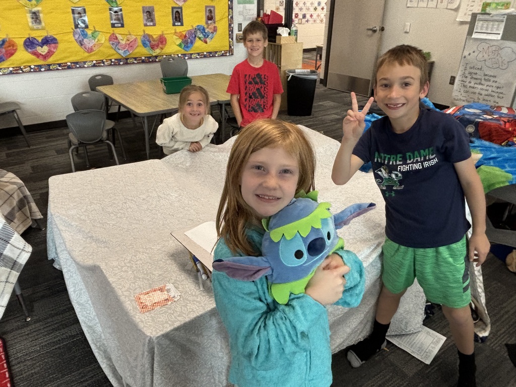 Two girls and two boys are standing next to their blanket fort smiling.