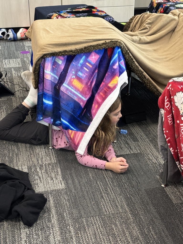 A girl lays under a blanket fort.