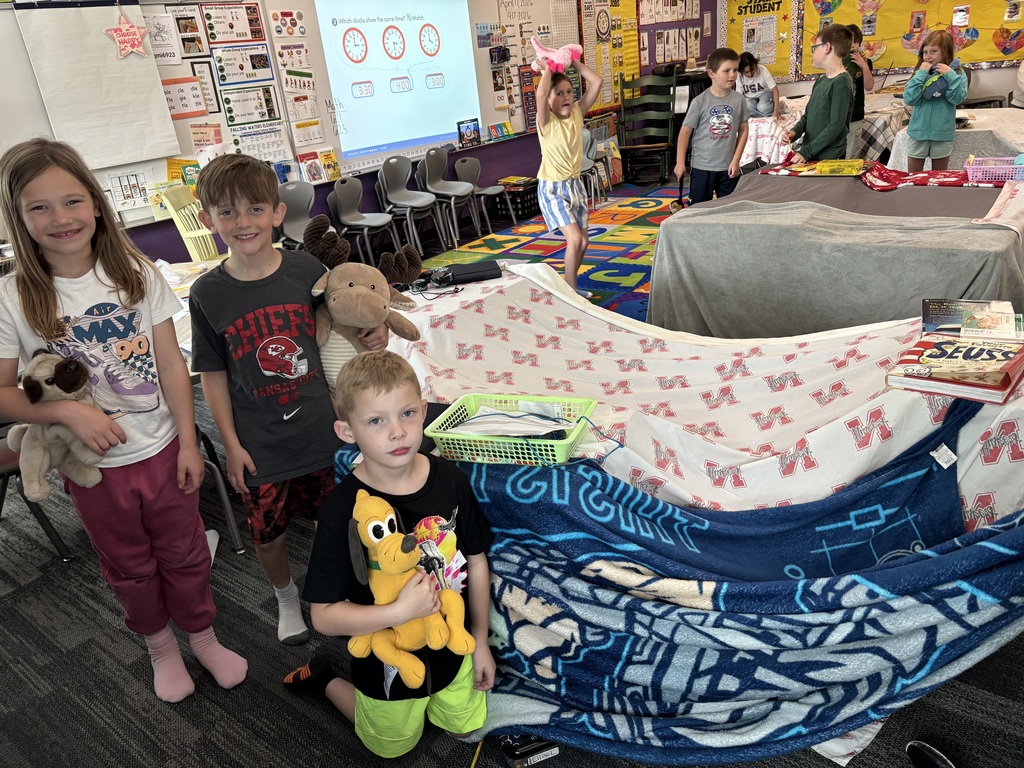 A girl and two boys hold stuffed animals standing next to a blanket fort.
