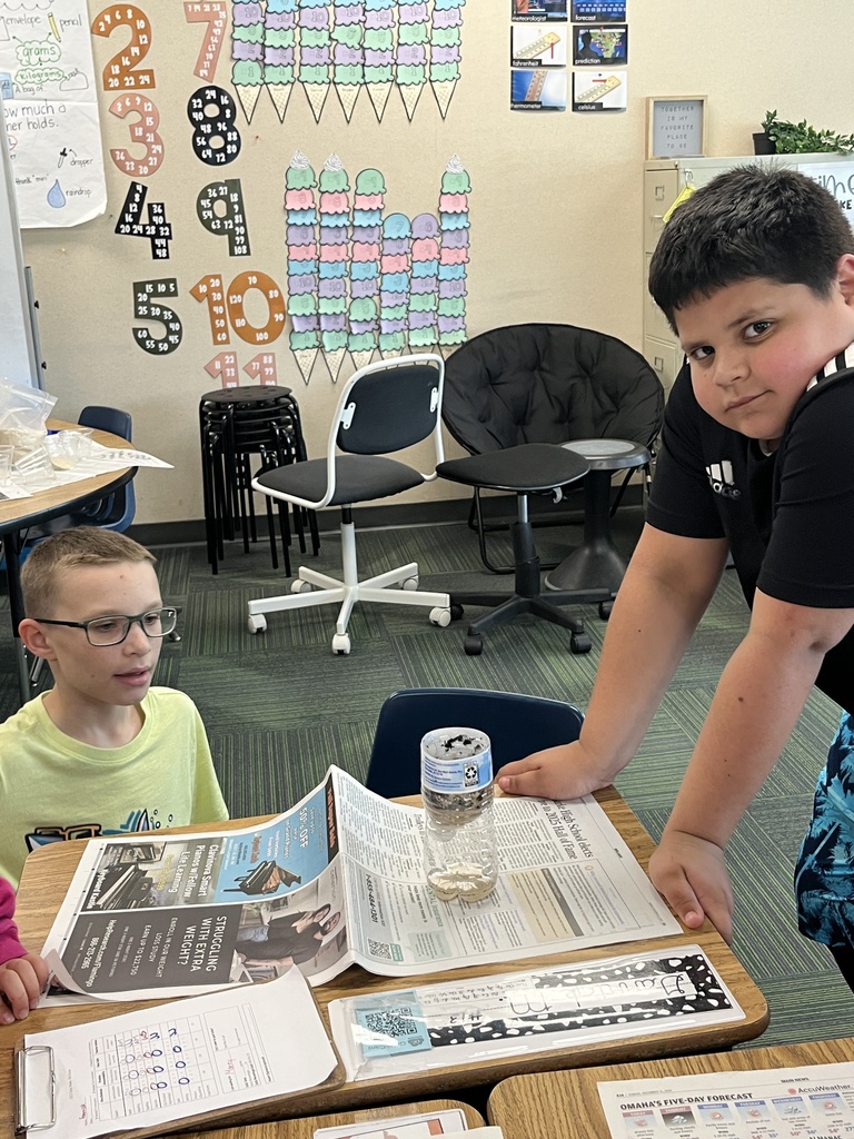 A boy in a yellow shirt and a boy in a black Adidas shirt stand over their desk featuring a plastic bottle filter and a weather observation chart.