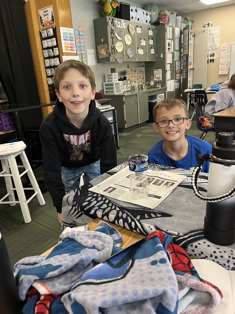 Two boys pose in a classroom; one wears a black "FNAF" hoodie while their project sits on a grey patterned towel.