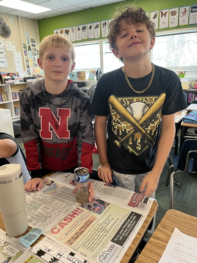 Two boys stand behind their project; one wears a Nebraska hoodie and the other a baseball-themed t-shirt and gold chain.