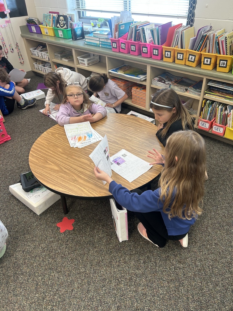 Students sitting down at a table and reading their writing to each other.