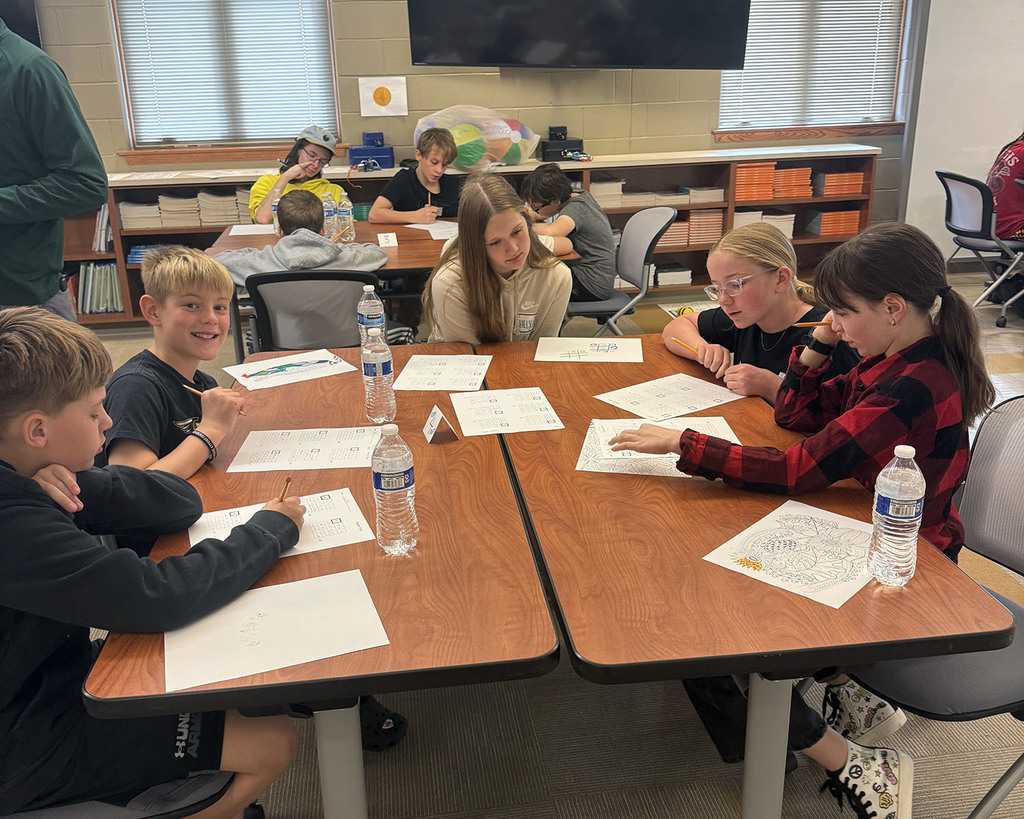 students sitting at a group of tables with worksheets collaborating on math problems