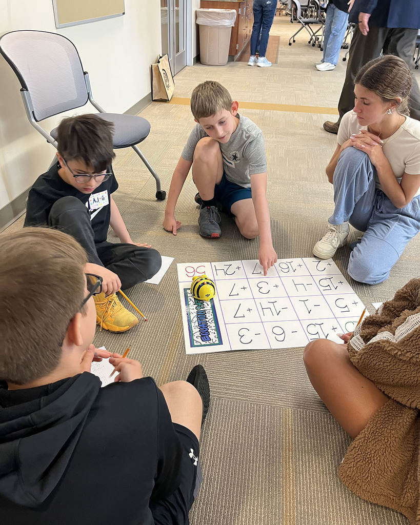 students sitting on the floor in a group around math solution chart and a robotic bee