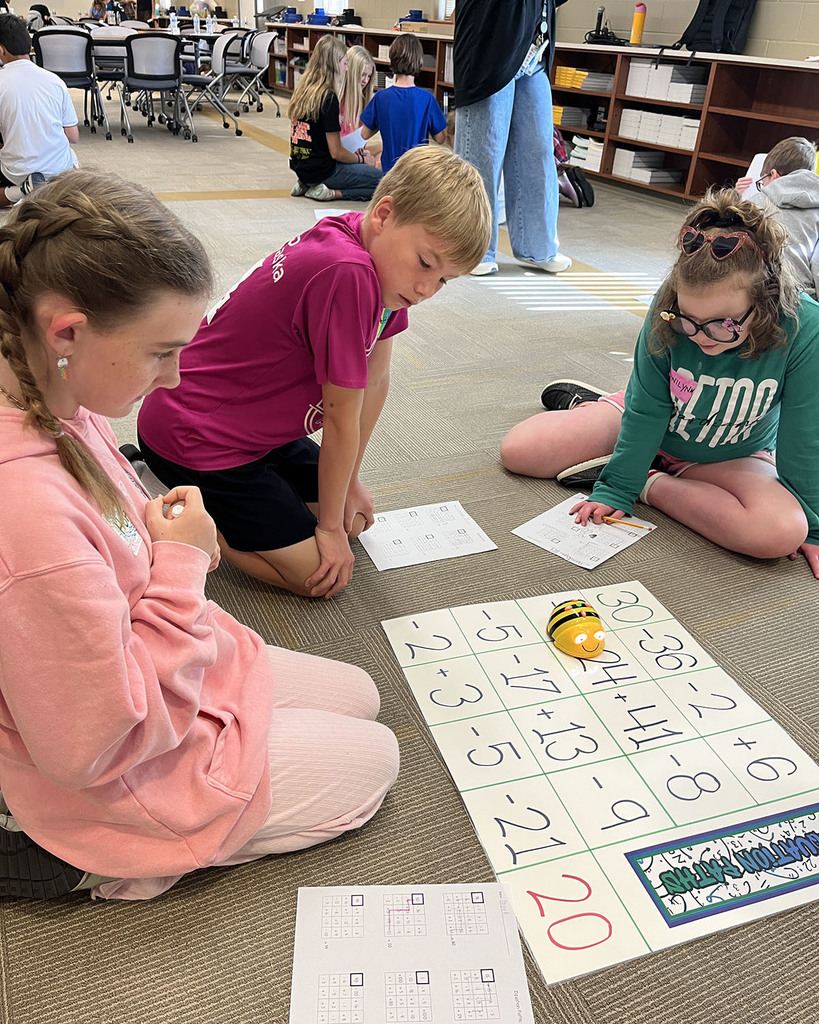 3 students sitting on the floor with a Math bee calculating their math answers