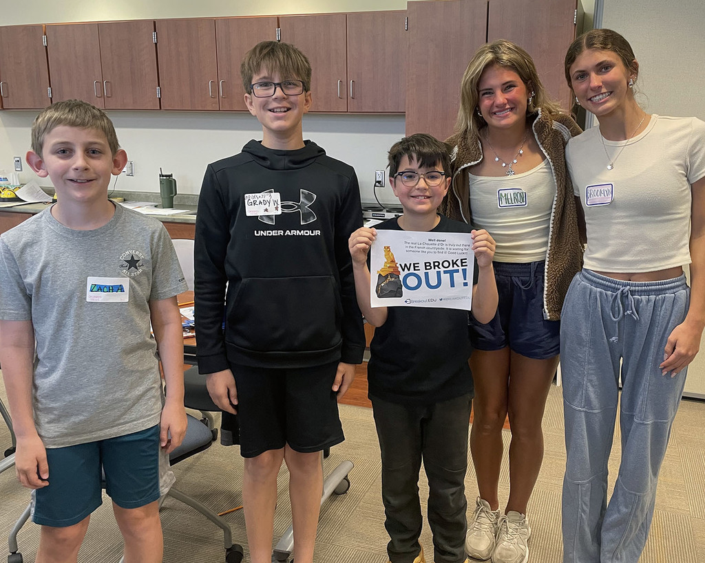 five students standing with smiles holding a "We Broke Out" after completing their math breakout session