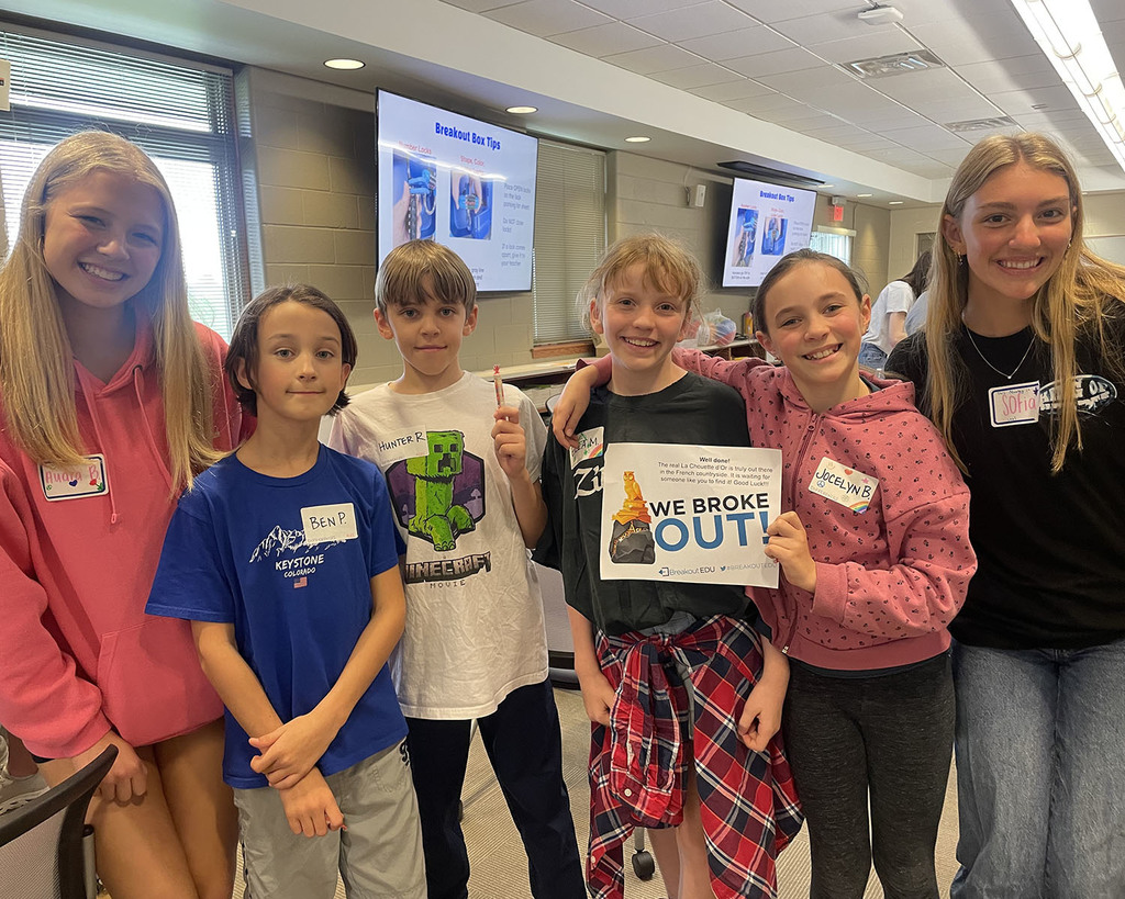 students smiling at the camera holding their "We Broke Out!" certificate after completing the math challenge