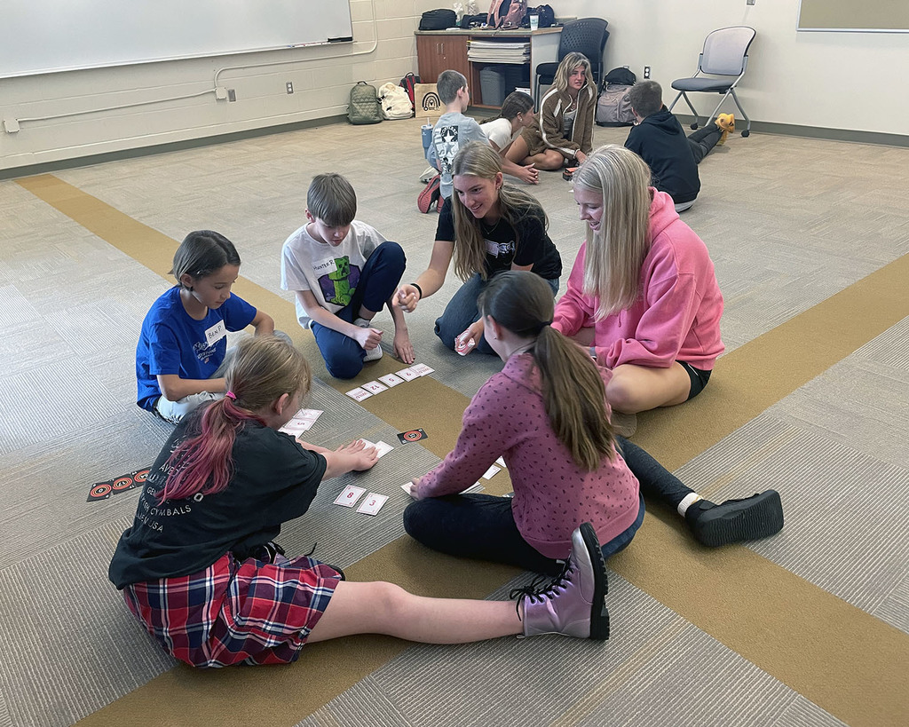 groups of students sitting on the floor playing a math card game