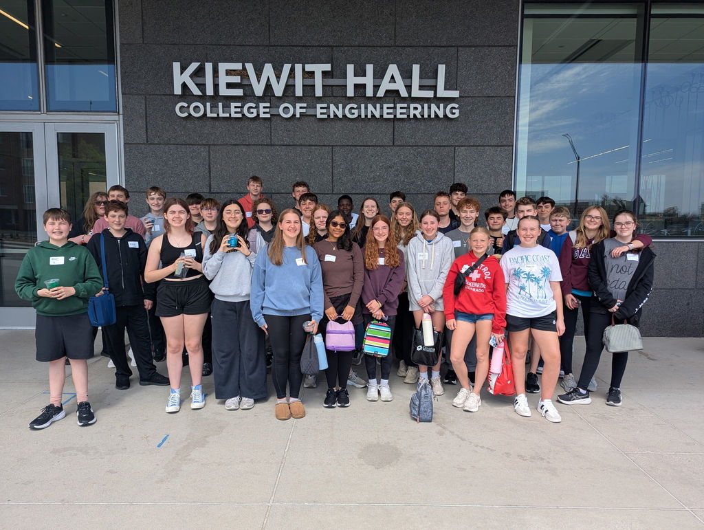 There are a bunch of students standing in front of the Kiewit Hall College of Engineering building. 
