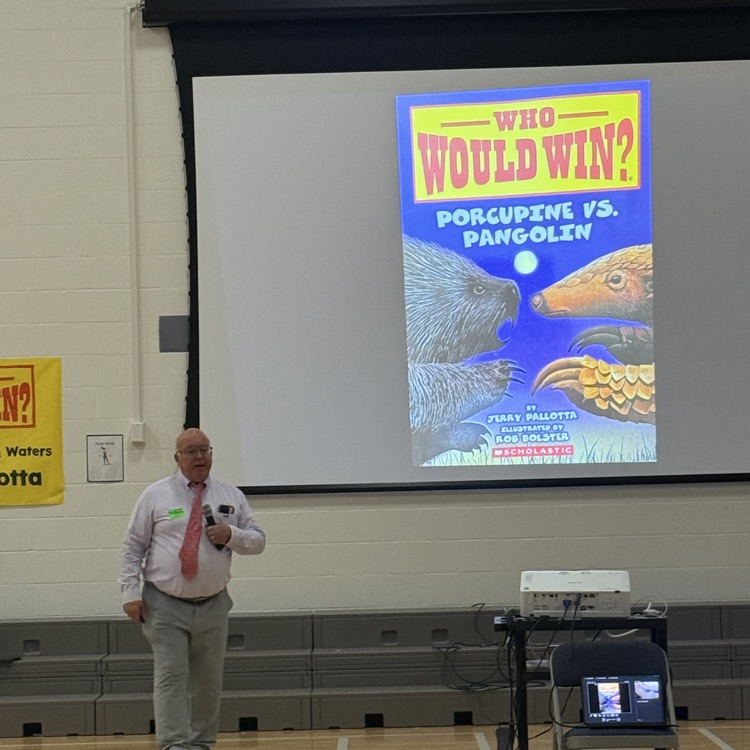 Jerry Pallotta stands next to a screen with the blue book cover for Who Would Win: Porcupine vs Pangolin?