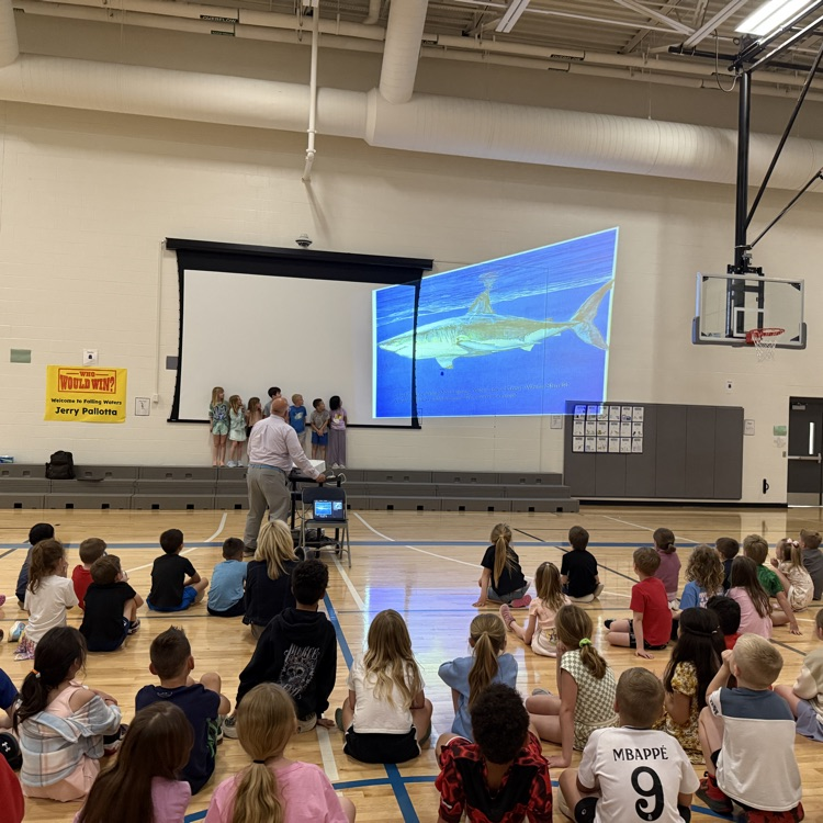 7 students stand in front of a screen while Jerry Pallotta moves a shark picture over them  