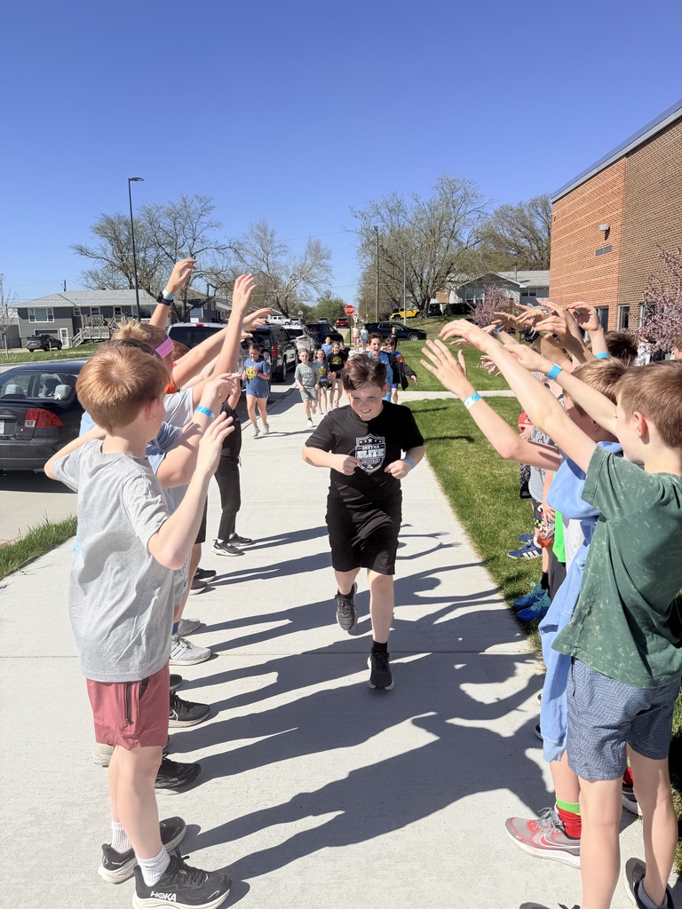 A boy in a black t-shirt runs down a sidewalk through a "tunnel" created by two rows of other children holding their arms up.