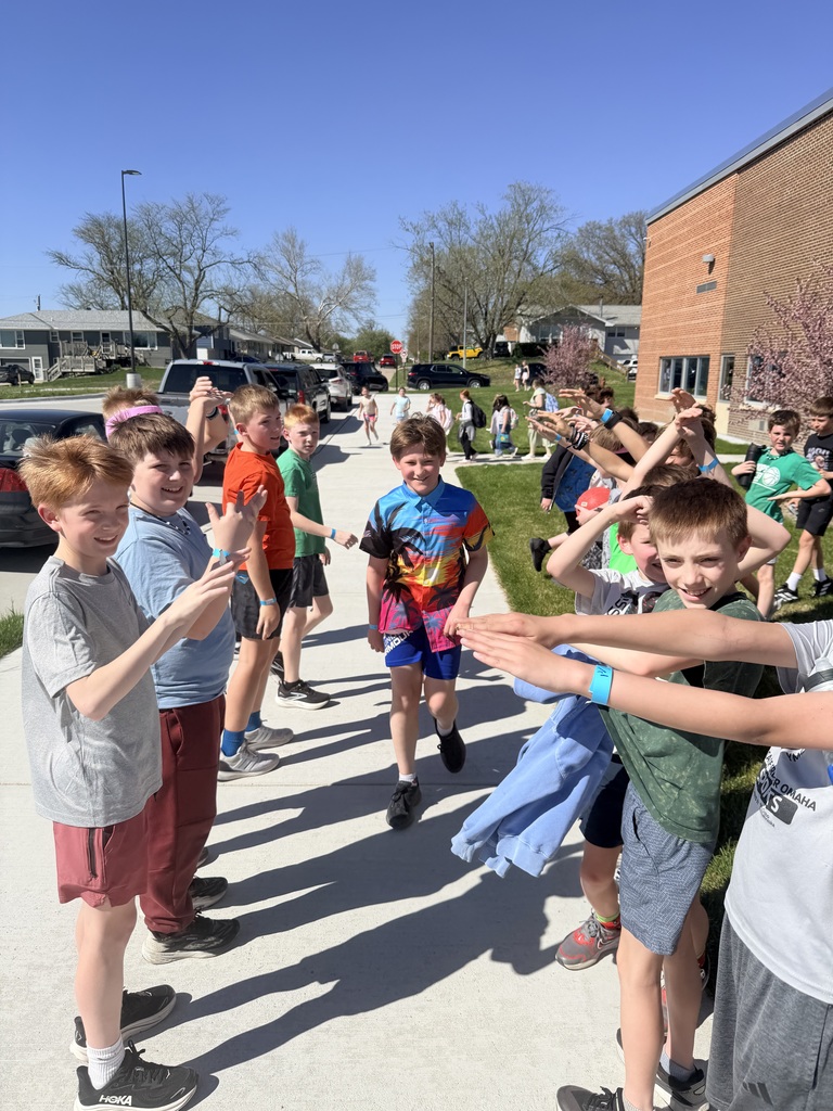 A boy in a colorful tropical shirt smiles as he walks through the cheering tunnel of peers on a sunny school day.