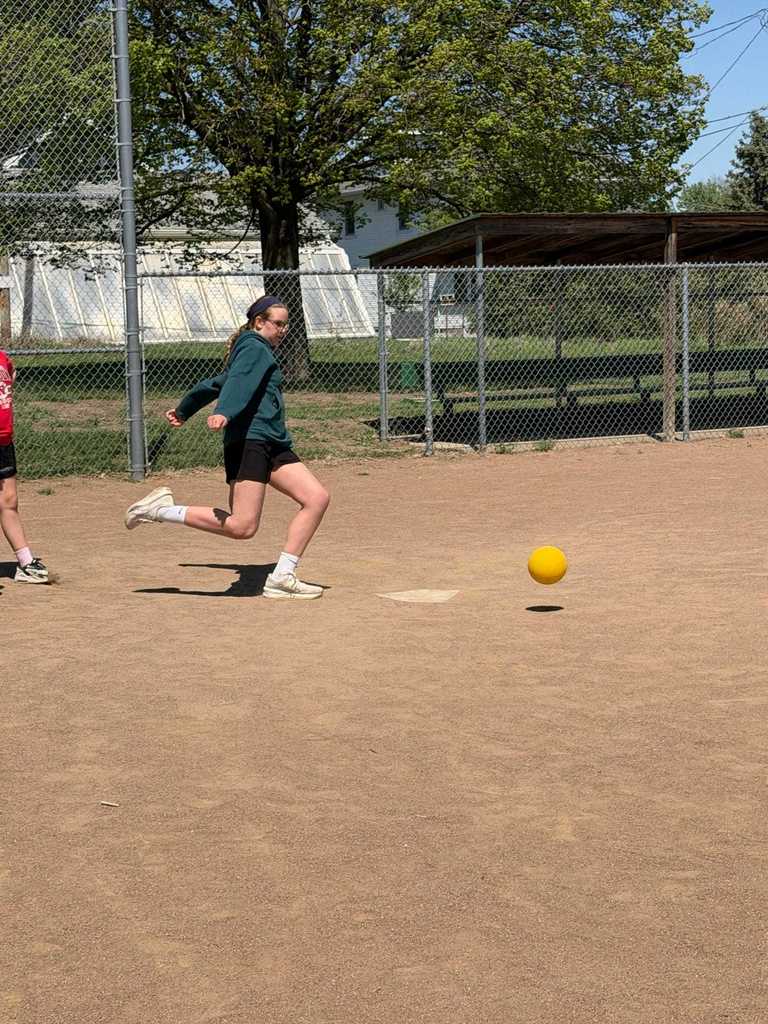 Action shot of a girl in a teal hoodie following through after kicking a yellow ball.
