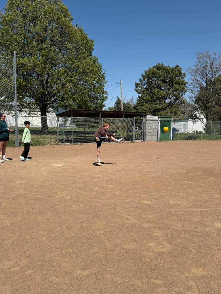 A boy in a brown hoodie mid-kick, sending a yellow ball into the air.