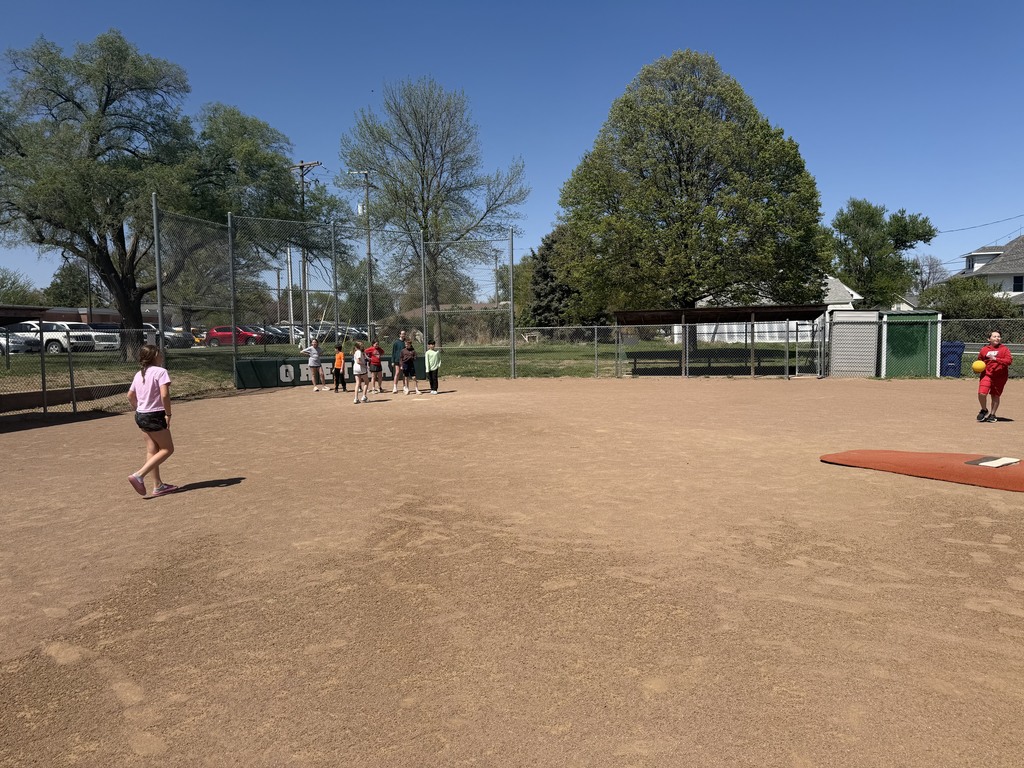 Wide view of children playing kickball on a large dirt field under a clear blue sky.