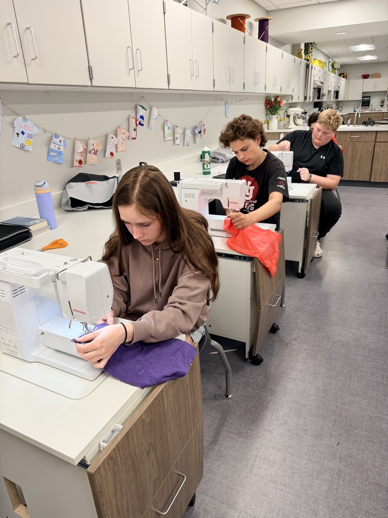 Three students sit at sewing machines sewing. 