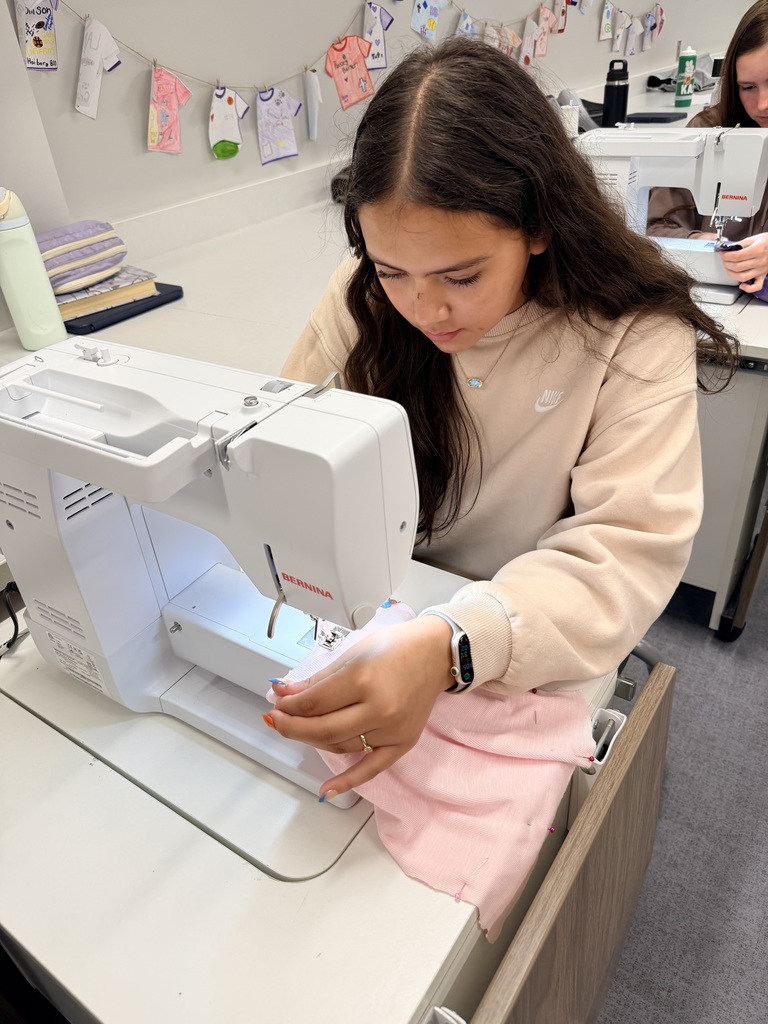 A female student sits at a sewing machine sewing. 
