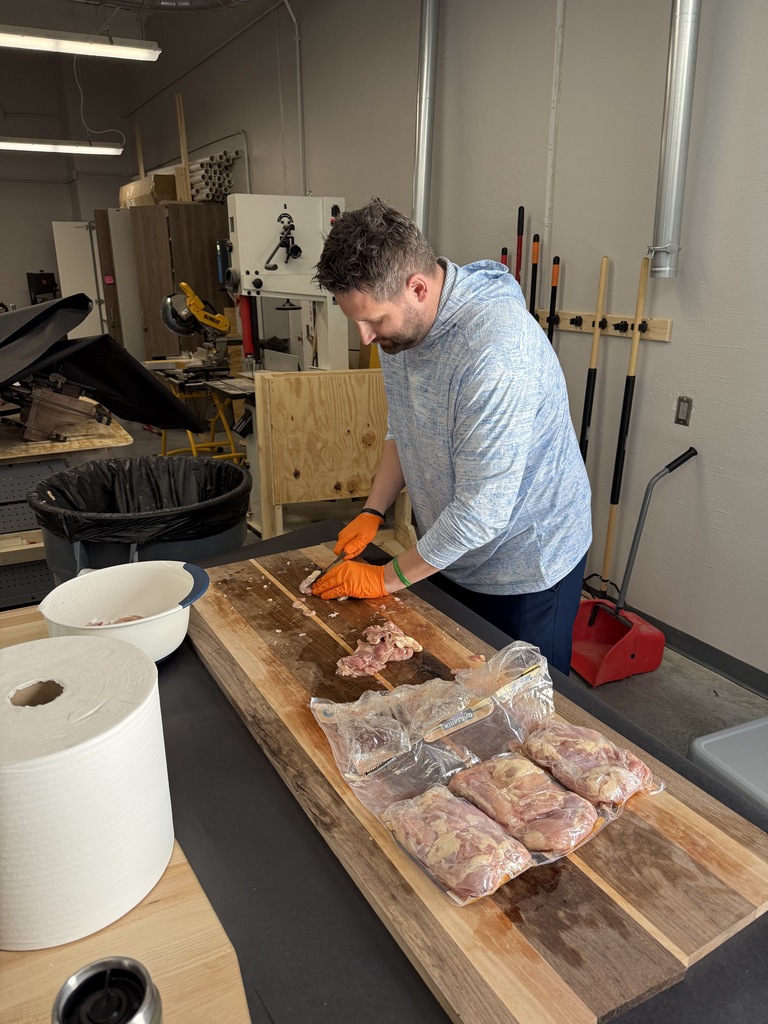 A man is cutting up chicken to be grilled. 