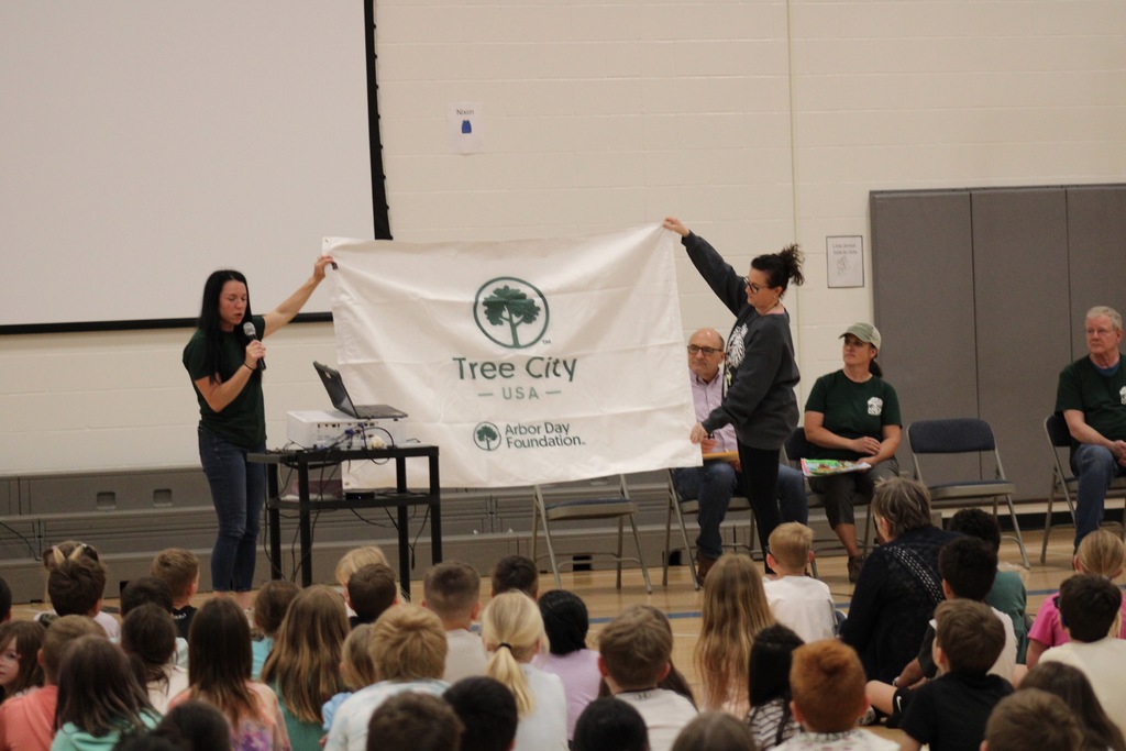 Mrs. Gabriel and the Arbor Day Foundation Tree Board president hold a white flag with a green logo for Tree City USA by Arbor Day Foundation.