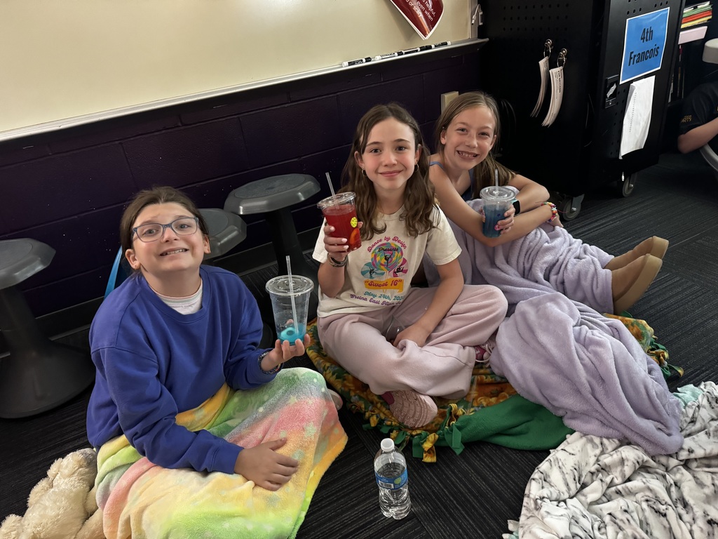 Three girls sitting on the floor wrapped in blankets, smiling and holding blue and red drinks.