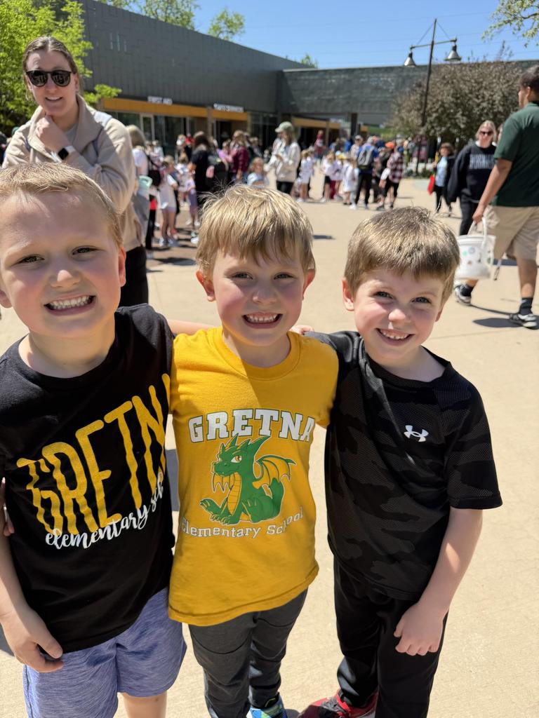 Close-up of three young boys smiling and arms around each other; the center boy wears a yellow shirt with a green dragon mascot.