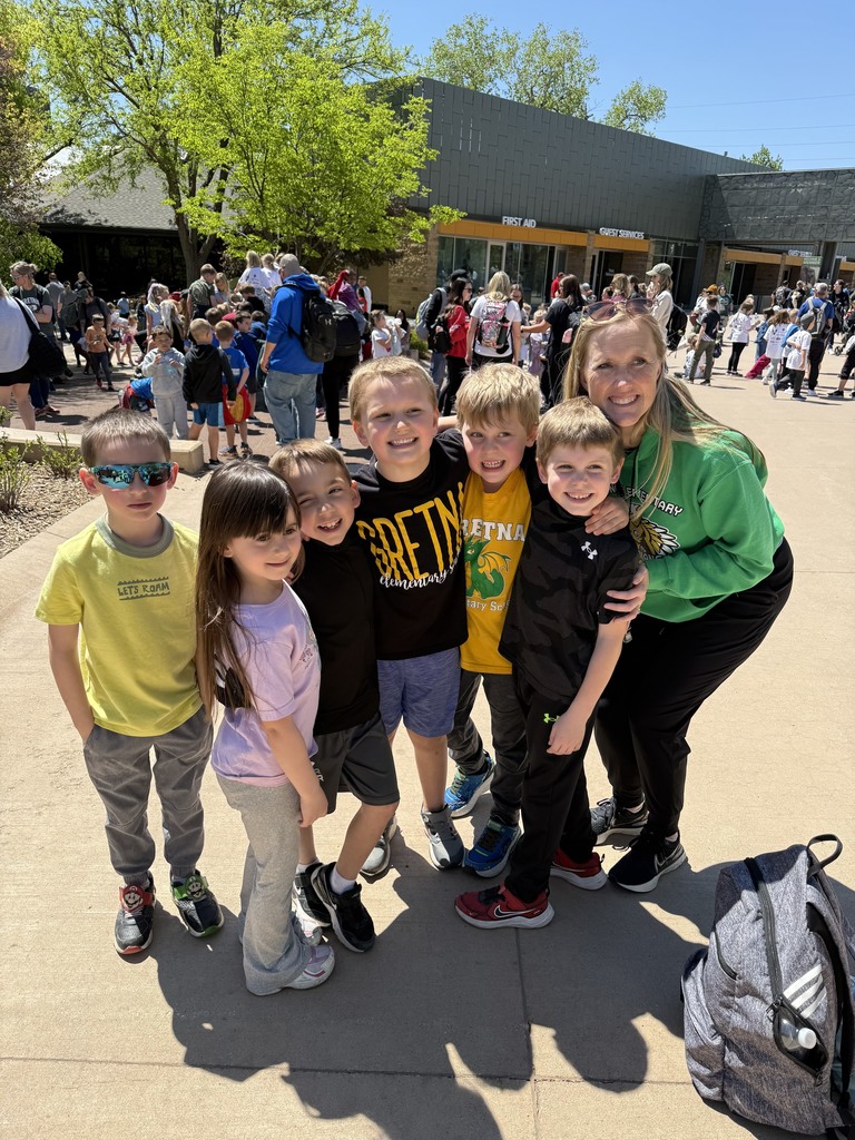 A group of six children and a smiling woman in a green "Gretna Elementary" hoodie pose together outdoors on a sunny day at the zoo.