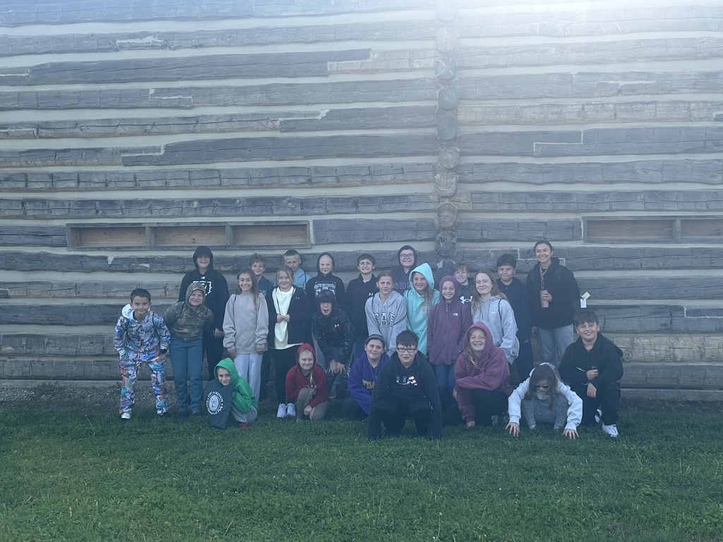 students posing in front of a log cabin