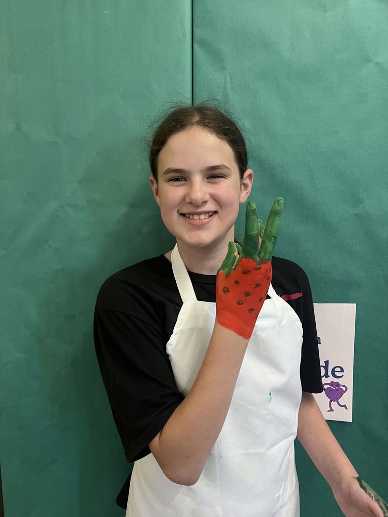 A girl smiling at the camera with her hand painted like a strawberry. 