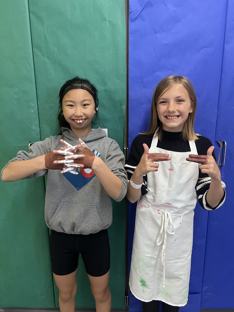 Two girls smiling at the camera with her hands painted like footballs. 