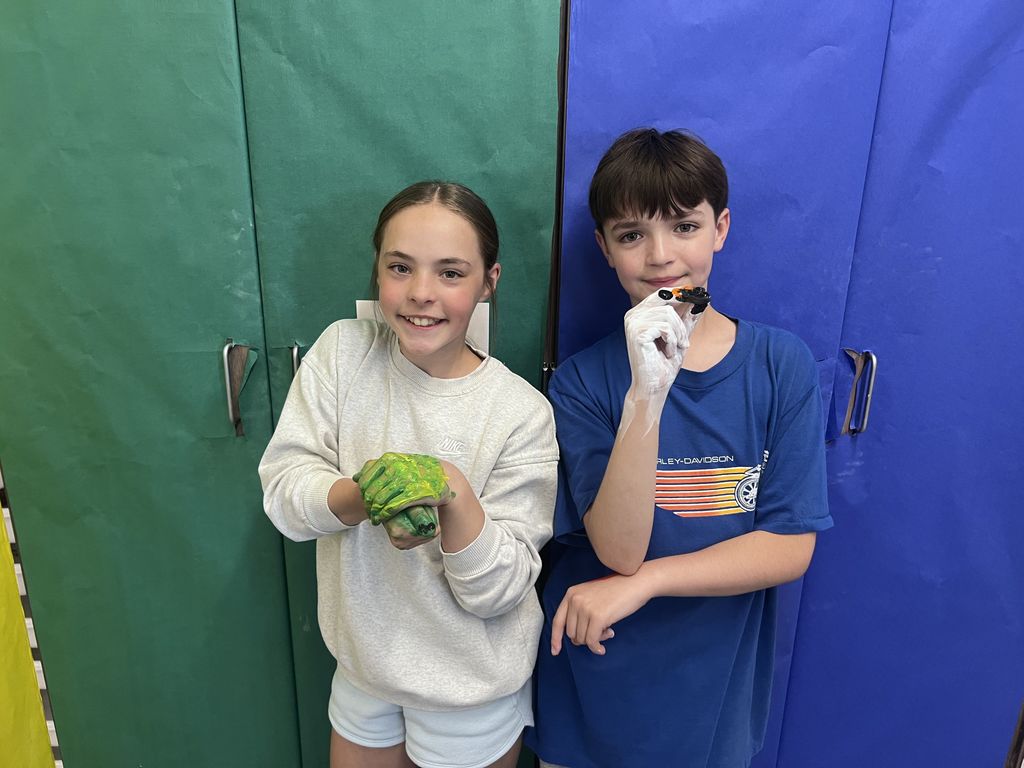 Two kids smiling at the camera with their hands painted. 