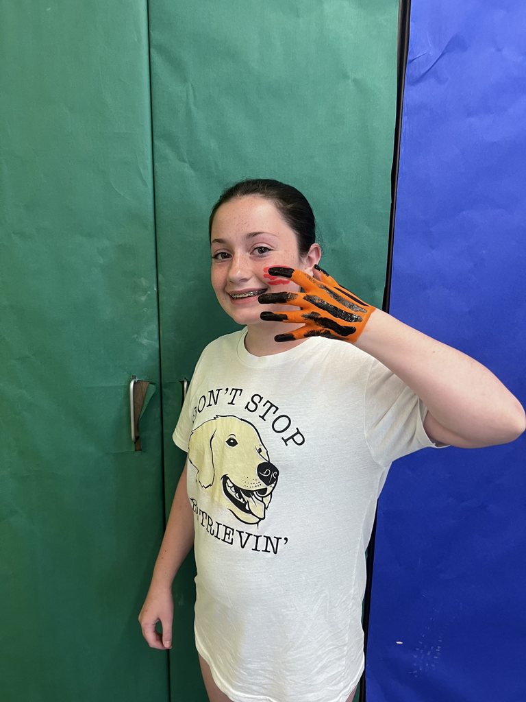 A girl smiling at the camera with her hand painted like a tiger. 