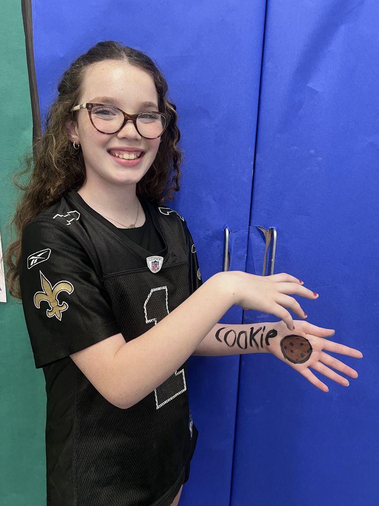 A girl smiling at the camera with a cookie painted on her hand. 
